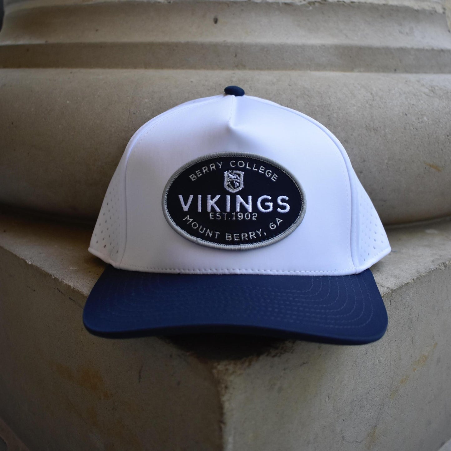 A white and navy blue baseball cap with a circular 'Berry College Vikings' patch on the front