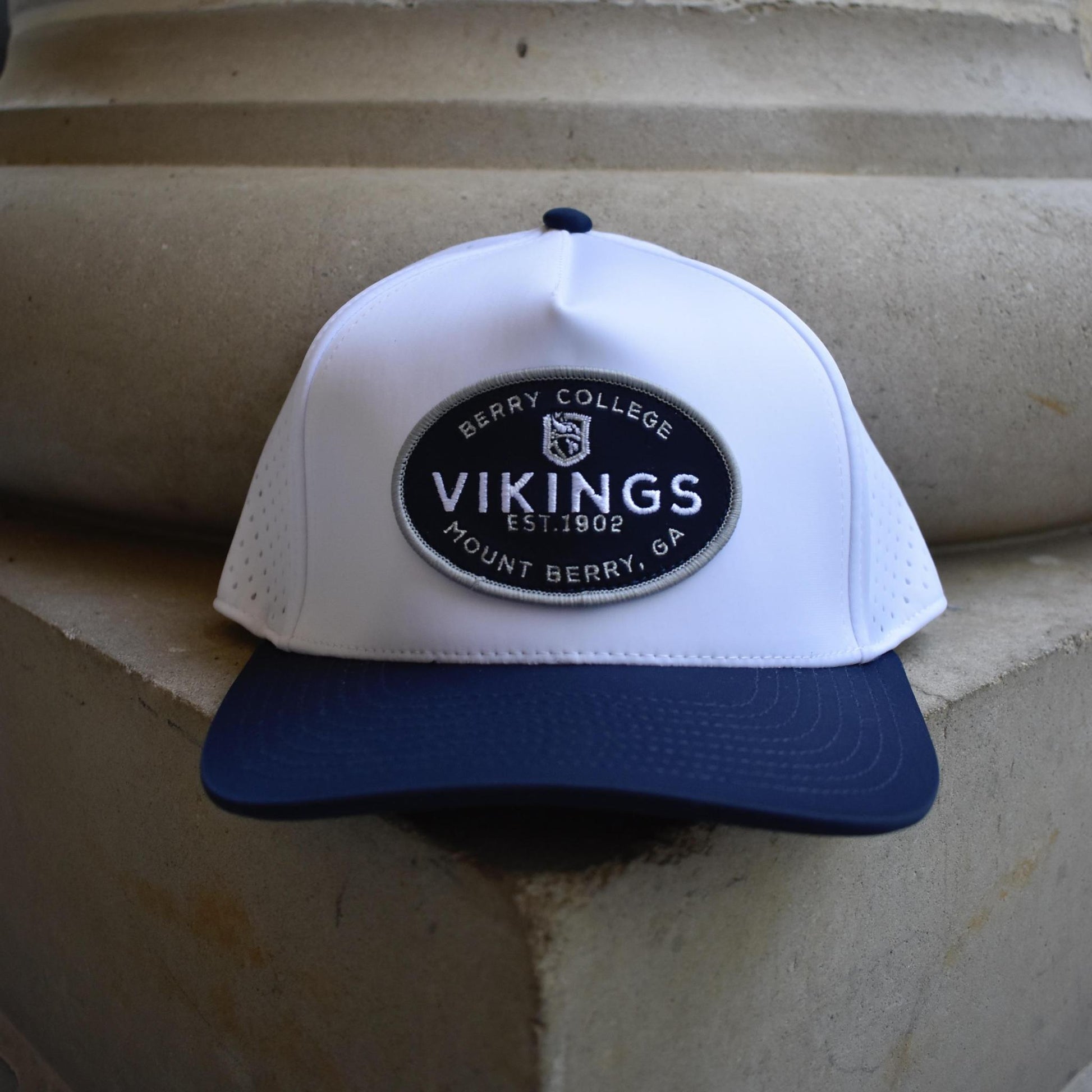 A white and navy blue baseball cap with a circular 'Berry College Vikings' patch on the front