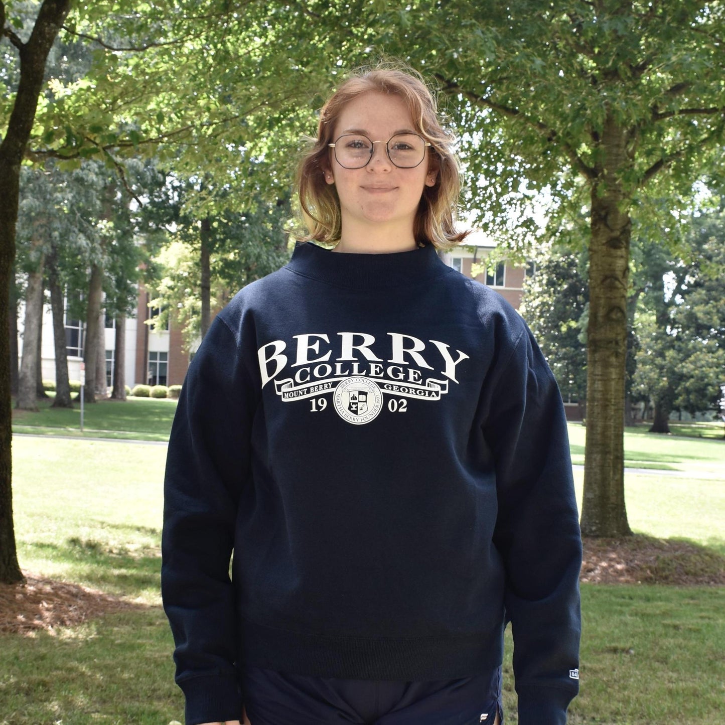 girl wearing a navy berry college mock neck with a banner and the college seal