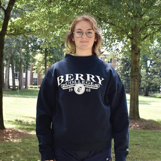 girl wearing a navy berry college mock neck with a banner and the college seal