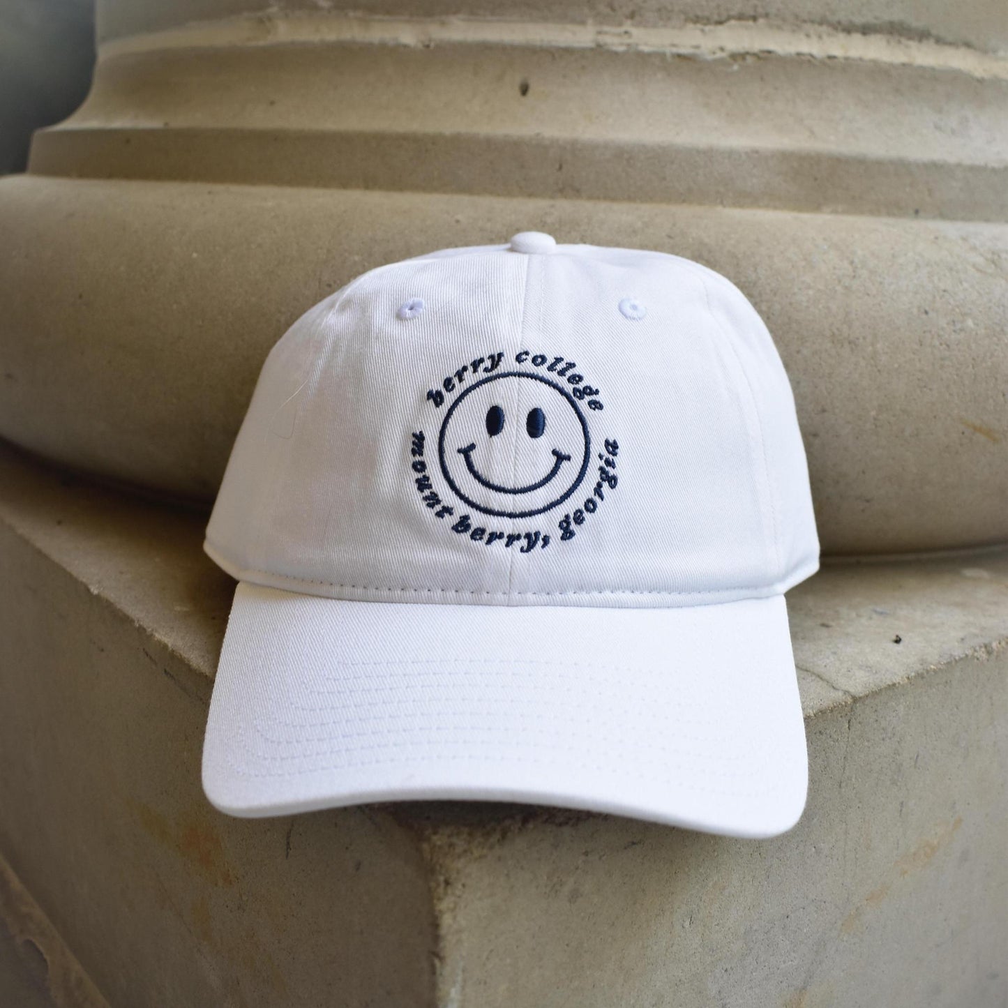 A white baseball cap with a black embroidered smiley face and the text 'berry college in myr Barry, Georgia' 